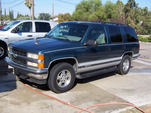 1995 Chevrolet Tahoe - A dark green SUV is parked on a concrete surface next to a silver pickup truck.