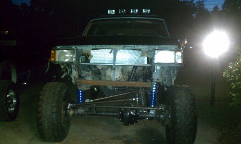 1990 Ford Bronco - Front view of a heavily modified truck with off-road suspension and large tires, lacking its grille and bumper.