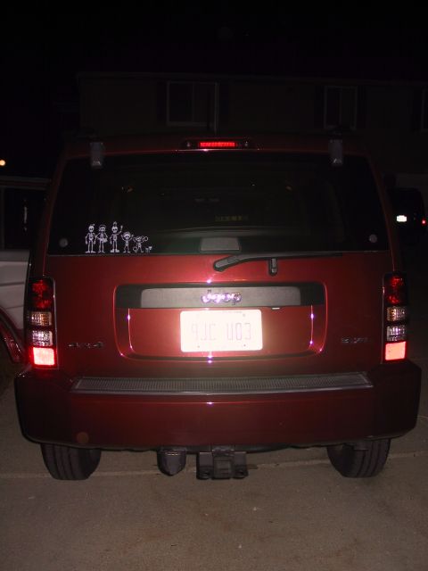 2008 Jeep Liberty - The rear of a red Jeep Liberty SUV is shown at night, a license plate and a family sticker on the rear window.