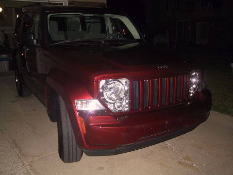 2008 Jeep Liberty - A red 2008 Jeep Liberty is parked in a driveway at night, showing its distinctive front grille and headlights.