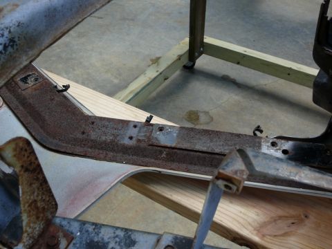 1976 Chevrolet Corvette - A close-up view shows a section of a car's frame with significant rust, resting on wooden supports.