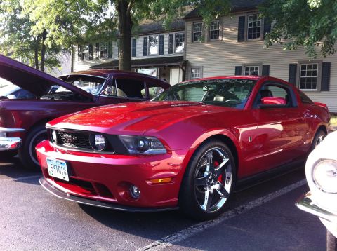 2010 Ford Falcon - A red Ford Mustang is parked at an outdoor car show, with another classic car visible beside it.