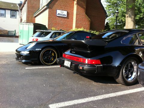 2010 Ford Falcon - Two black Porsche 911s are parked side-by-side with a white SUV in the background.