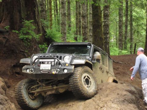 2008 Jeep Wrangler - A black Jeep Wrangler navigates a muddy trail in a dense forest with a person observing.