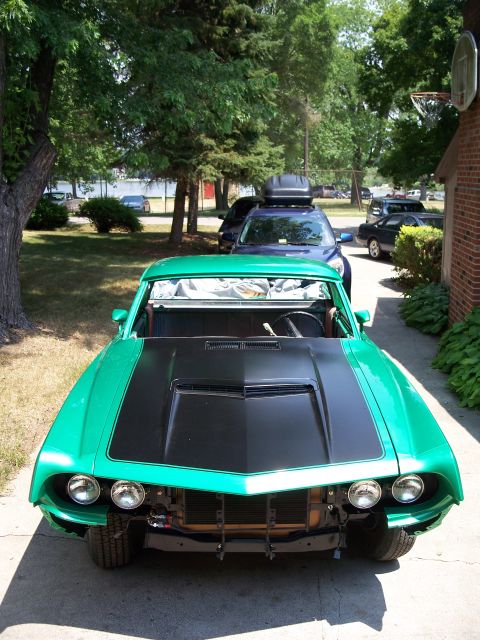 1971 Ford Ranchero - A green muscle car is parked in a driveway, showing its front end with a black hood scoop and exposed grille.