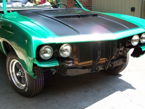 1971 Ford Ranchero - A green car with a black hood and scoop is shown from the front, with its bumper and grille removed.