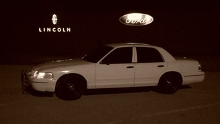 1998 Ford Crown Victoria - A white 1998 Ford Crown Victoria is parked at night, with Ford and Lincoln dealership signs visible in the background.
