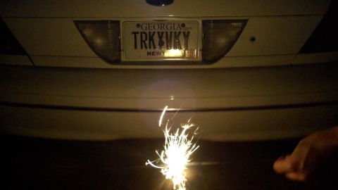 1998 Ford Crown Victoria - A sparkler is lit below the rear of a 1998 Ford Crown Victoria, which displays a Georgia license plate.