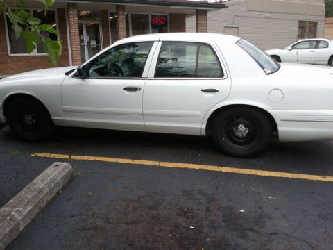 1998 Ford Crown Victoria - A white 1998 Ford Crown Victoria sedan is parked in a lot, with another similar vehicle visible in the background.