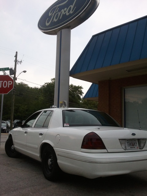 1998 Ford Crown Victoria - A white sedan is parked in front of a Ford dealership, with a stop sign visible in the background.