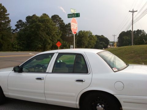 1998 Ford Crown Victoria - A white 1998 Ford Crown Victoria sedan is parked near an intersection with street signs and a stop sign.
