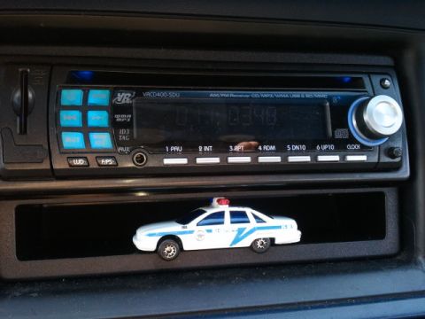 1998 Ford Crown Victoria - A toy police car sits in the dashboard compartment of a vehicle, below the car stereo.