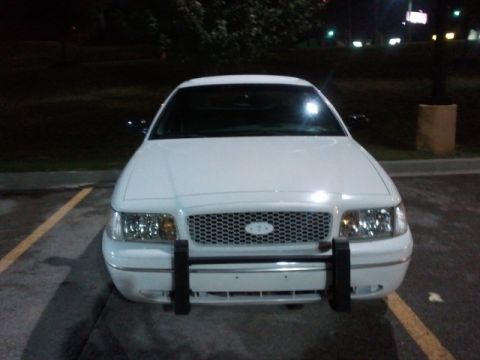 1998 Ford Crown Victoria - A white Ford Crown Victoria with a push bar is parked in a lot at night, viewed from the front.