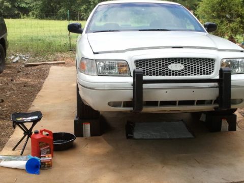 1998 Ford Crown Victoria - A white 1998 Ford Crown Victoria is parked on blocks, ready for maintenance, with a push bar on the front.