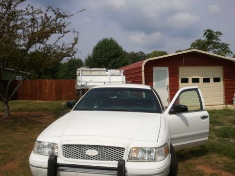 1998 Ford Crown Victoria - Front view of a white 1998 Ford Crown Victoria with the driver's door ajar, parked outside a red garage.