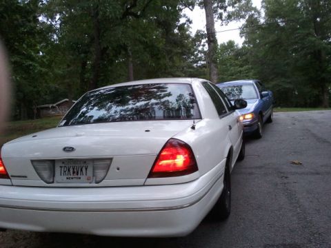 1998 Ford Crown Victoria - Two sedans are parked on a road with trees in the background. The white car is in the foreground.