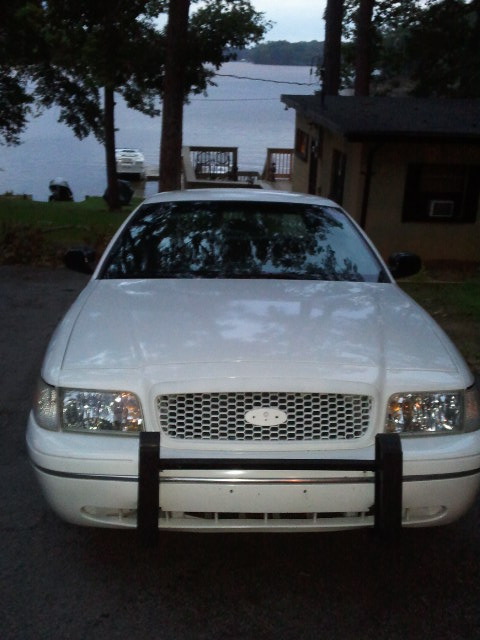 1998 Ford Crown Victoria - A white 1998 Ford Crown Victoria is parked in front of a house by a lake.