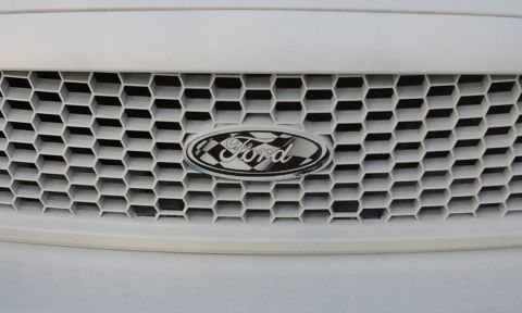1998 Ford Crown Victoria - A close-up of a white Ford grille with a honeycomb pattern and an oval Ford emblem featuring a checkered flag background.