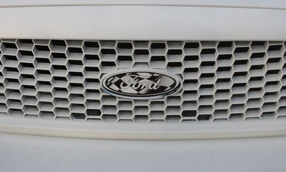 Close-up of a white Ford grille with honeycomb pattern and Ford emblem with checkered flag.