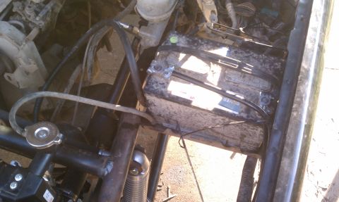 1990 Ford Bronco - Close-up view of a vehicle's engine bay, focusing on the battery and radiator cap.