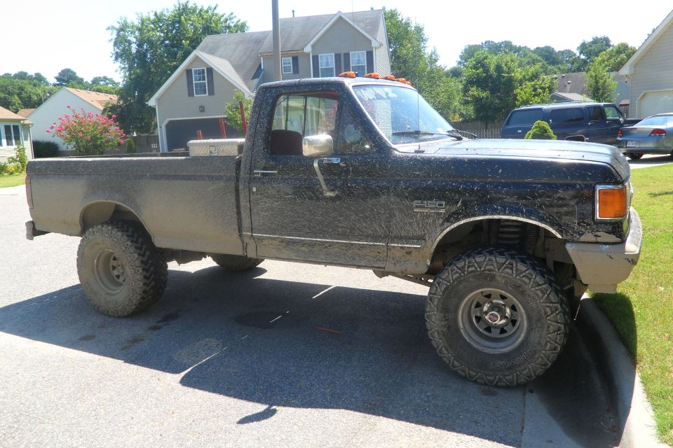 Mud-covered pickup truck parked on a street. It has large tires and a toolbox in the bed