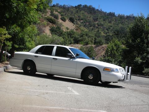 2004 Ford Crown Victoria - A white sedan, possibly a 2004 Ford Crown Victoria, is parked in a lot with a push bumper attached to the front.