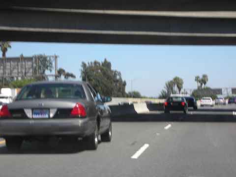 2004 Ford Crown Victoria - A dark gray 2004 Ford Crown Victoria is seen from behind on a sunny day, driving on a highway with other vehicles.