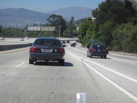 2004 Ford Crown Victoria - A dark blue Ford Crown Victoria Police Interceptor is seen from behind on a sunny day on the highway.