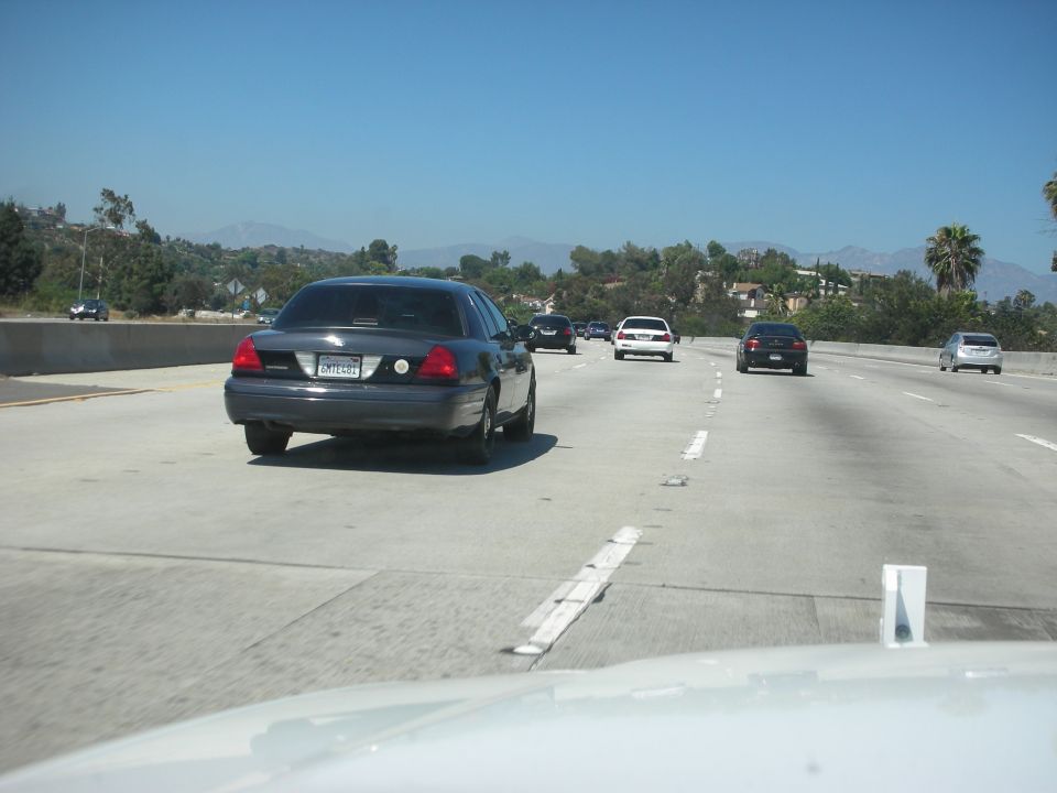 Dark sedan, 2004 Ford Crown Victoria, on highway, rear view, license plate visible