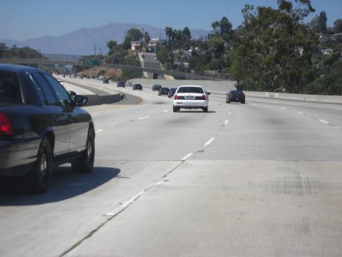 2004 Ford Crown Victoria - A black police car is seen driving on the highway alongside other vehicles.