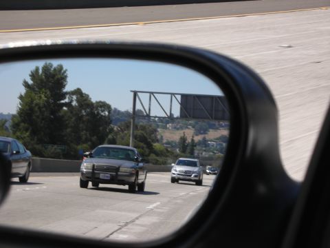 2004 Ford Crown Victoria - A police car is seen in the side mirror while driving on a sunny day on the highway.