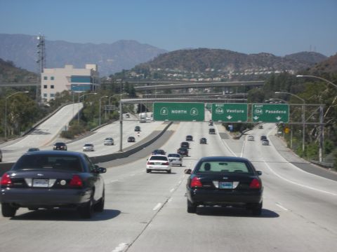 2004 Ford Crown Victoria - Multiple vehicles on a multi-lane highway under a clear blue sky with mountains in the background.