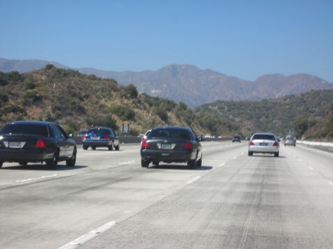 2004 Ford Crown Victoria - Multiple vehicles drive on a highway with mountains in the background.