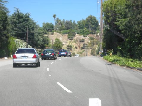 2004 Ford Crown Victoria - A line of cars, including a silver Ford Crown Victoria, travel up a winding road on a sunny day.