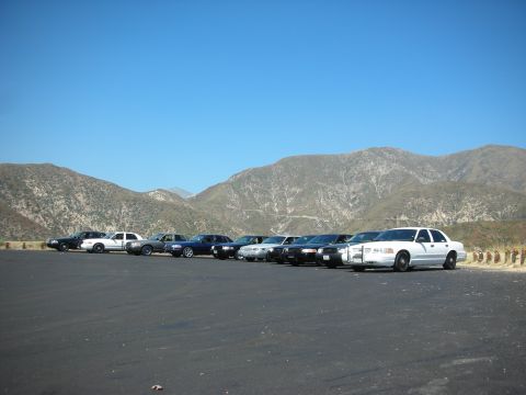 2004 Ford Crown Victoria - A fleet of police cars, including a white 2004 Ford Crown Victoria, are parked in front of a mountain range.