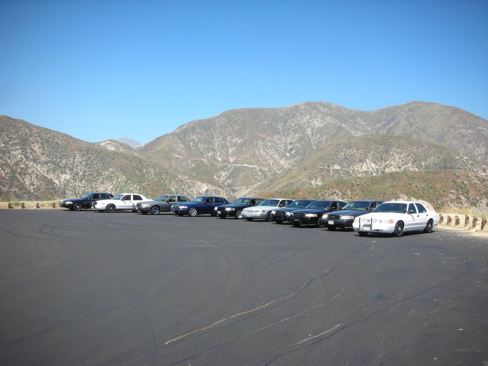 several sedans parked on asphalt with mountains behind them
