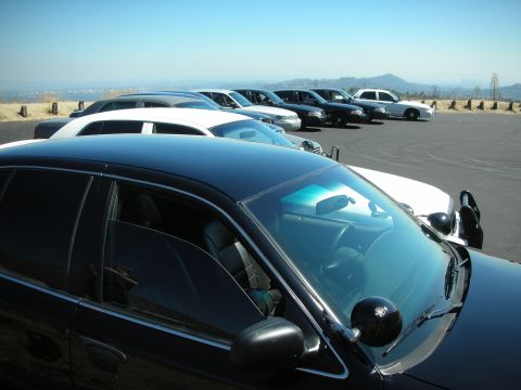 2004 Ford Crown Victoria - A fleet of police cars, including a black 2004 Ford Crown Victoria, are parked in a lot overlooking a city.
