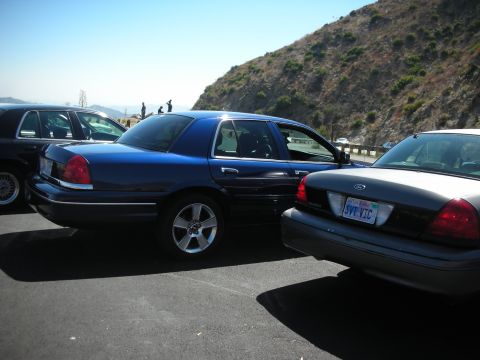 2004 Ford Crown Victoria - Two Ford Crown Victoria sedans are parked on a sunny day with a hillside in the background.