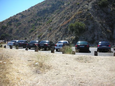 2004 Ford Crown Victoria - A line of Ford Crown Victorias, likely police vehicles, are parked in a dusty lot at the base of a rocky mountain.
