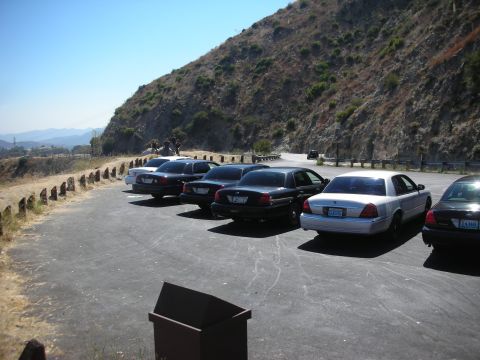 2004 Ford Crown Victoria - Several Ford Crown Victorias are parked in a lot next to a hillside.
