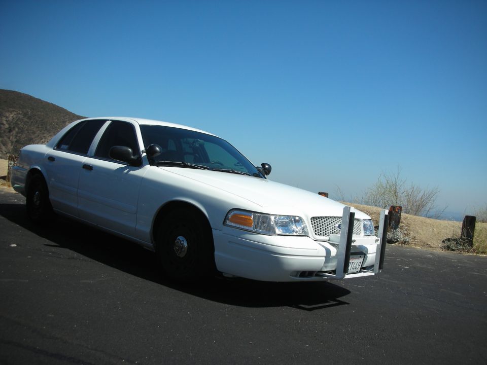 White 2004 Ford Crown Victoria police car with push bar parked on roadside
