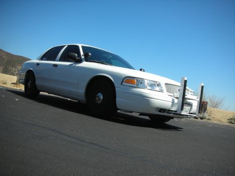 2004 Ford Crown Victoria - White police car with push bumper and California license plate 7T449 parked on asphalt under a clear blue sky.