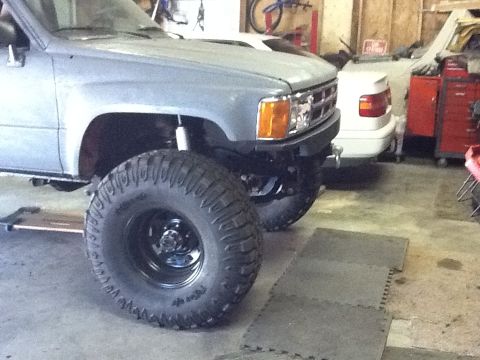 1988 Suzuki Samurai - Front view of a heavily modified pickup truck with oversized tires, parked indoors.