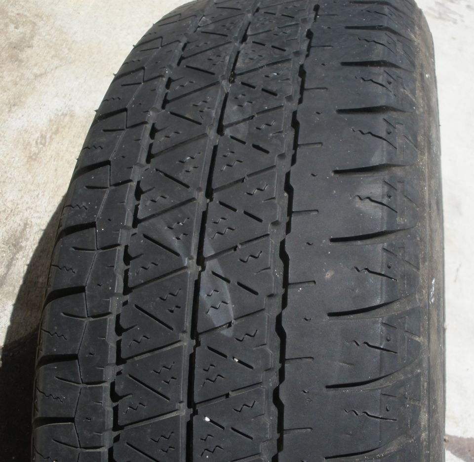 Tire tread with a zig-zag pattern and horizontal sipes, resting on a concrete surface