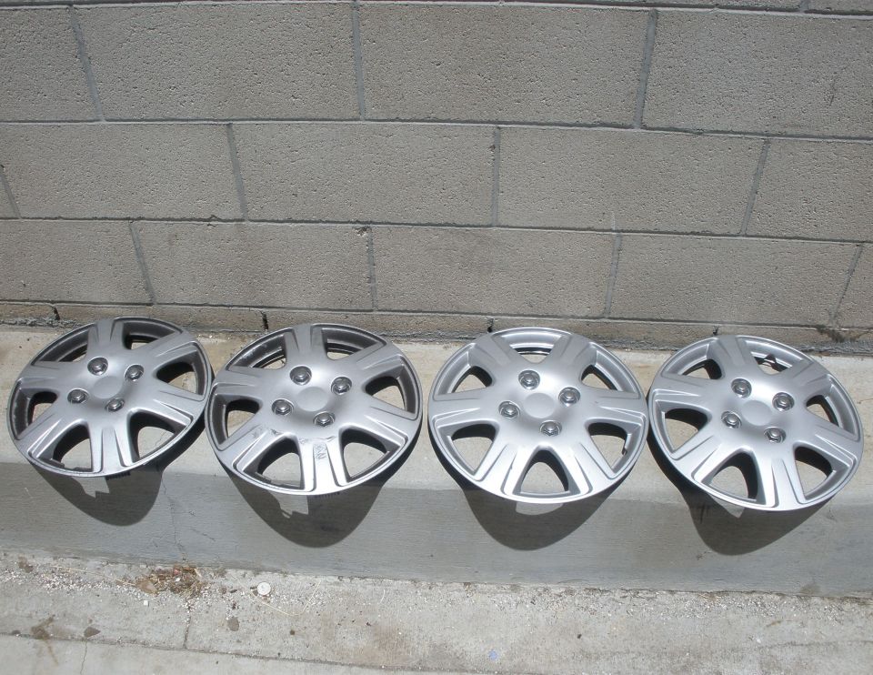 Four silver hubcaps lined up on a concrete surface in front of a brick wall