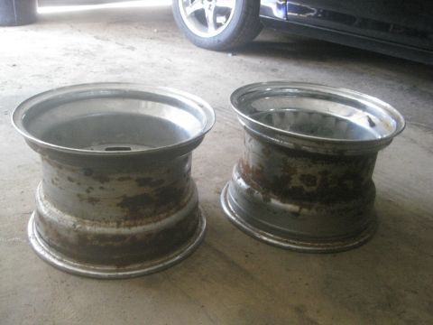 1995 Ford Ranger - A pair of aged aluminum wheels sit on a concrete surface, with a portion of a dark vehicle visible in the background.