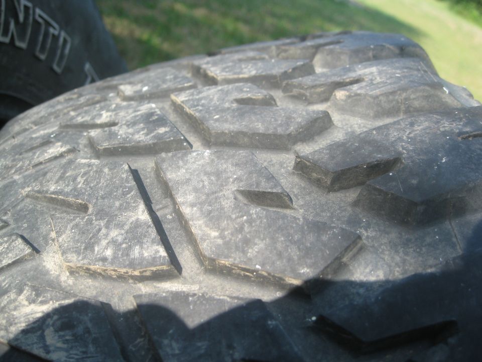 Close-up of aggressive off-road tire tread pattern. Text 'ANTI' visible on another tire in background