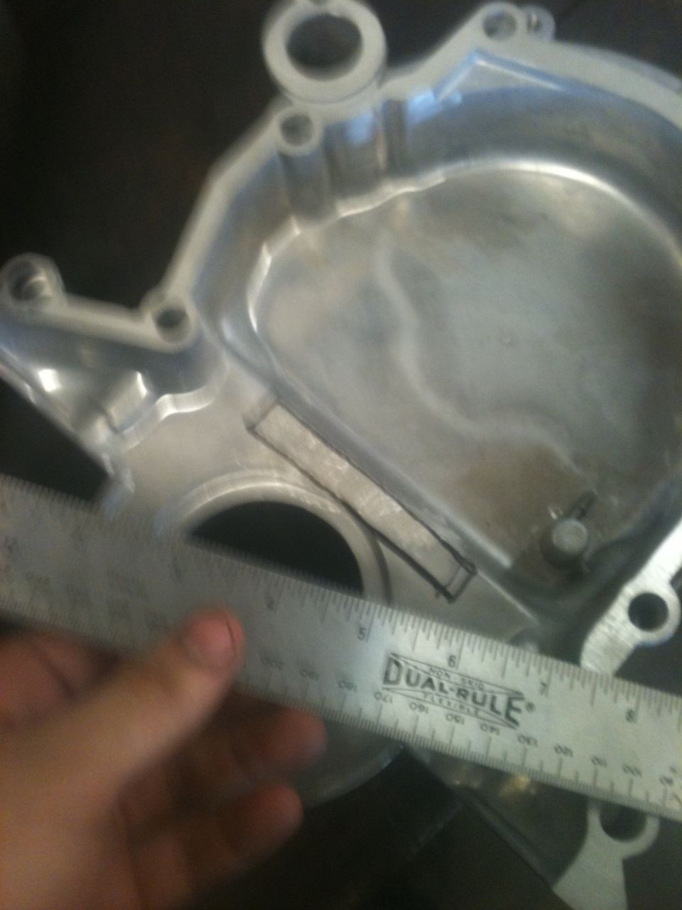 Close-up of an engine part with a ruler measuring a section. Text on ruler reads 'DUAL-RULE'
