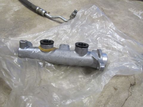 1995 Ford Bronco - A Ford brake master cylinder is shown, with a hose in the background and plastic packaging.