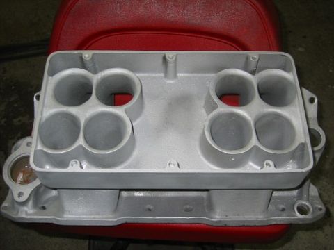 1953 Ford Mainline - An aluminum intake manifold with eight ports is shown from above, resting on a red seat.